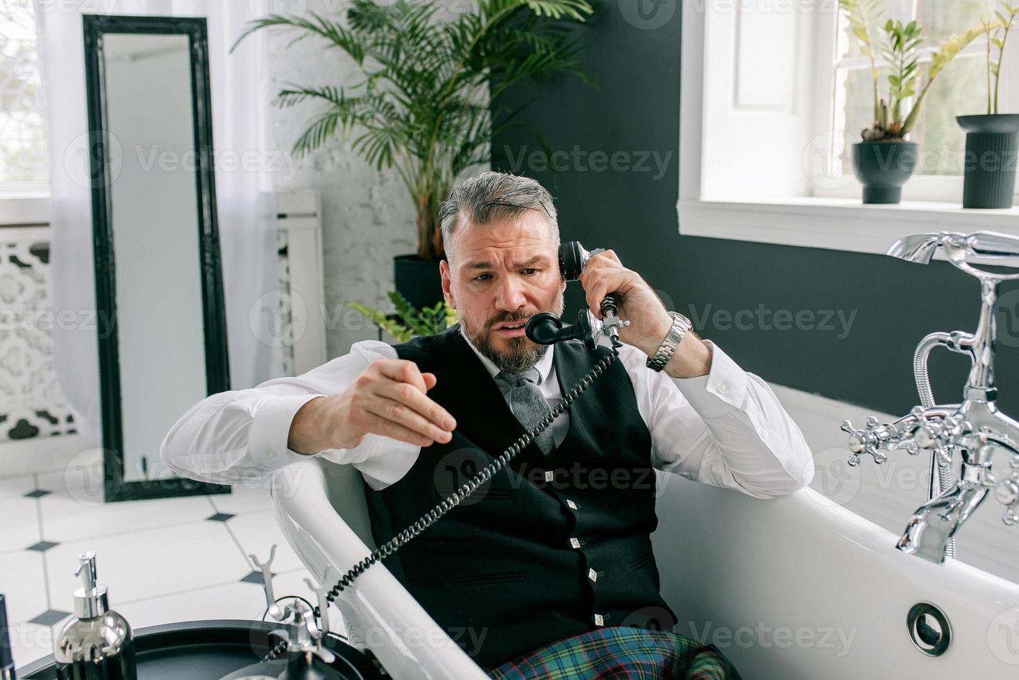 handsome mature courageous stylish man scotsman in kilt and suit talking on the phone from home. Style, fashion, lifestyle, lockdown, culture, ethnic concept. photo