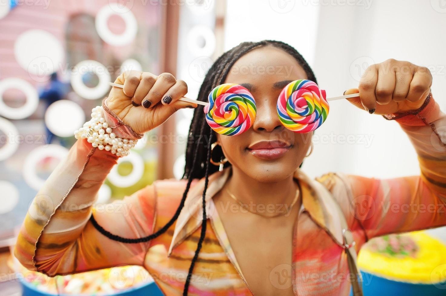 dama milenaria afroamericana en la tienda de dulces con piruletas que se cubren los ojos. foto