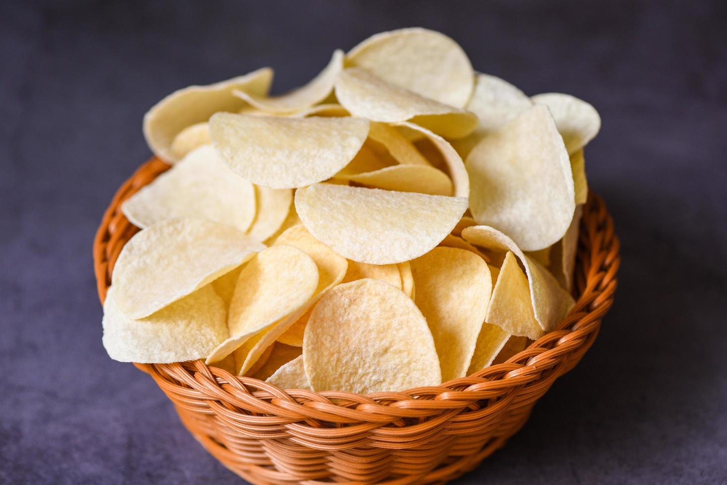 Potato chips snack on basket, Crispy potato chips on the kitchen table black background photo