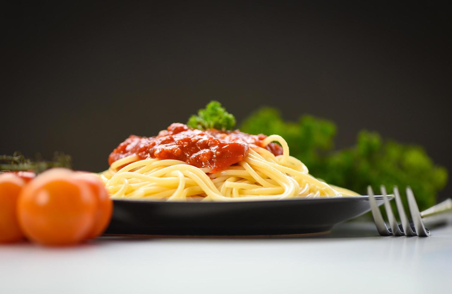 espaguetis pasta italiana servida en un plato negro con tomate y perejil en el restaurante comida italiana y concepto de menú - espaguetis a la boloñesa foto