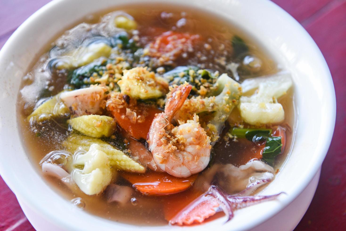 Thick Gravy seafood noodles with squid shrimp prawn and vegetable on bowl on wooden table background - photo