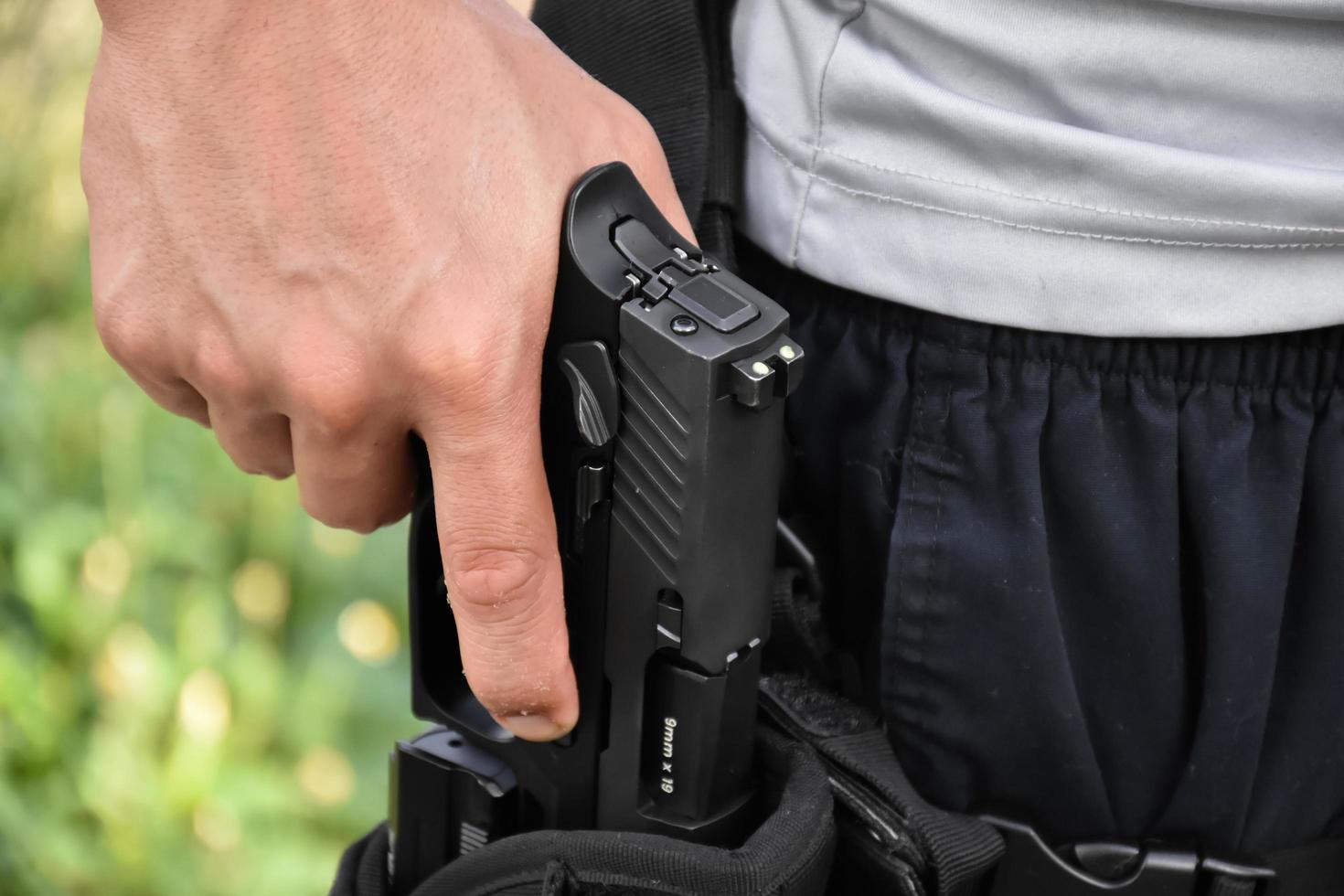 Pistola automática de 9 mm sujeta en la mano en la funda, lista para sacar y lista para disparar al objetivo por delante, concepto para la profesión de seguridad y deporte de tiro en todo el mundo. foto