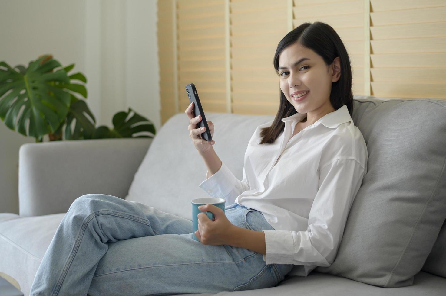 Young happy woman relaxing and using smart phone at home, social media and technology concept. photo