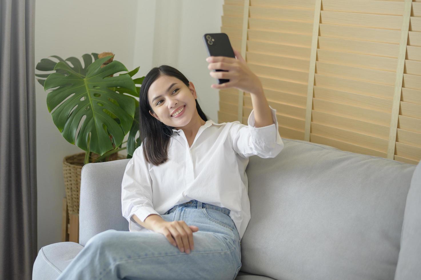 Young happy woman relaxing and using smart phone at home, social media and technology concept. photo