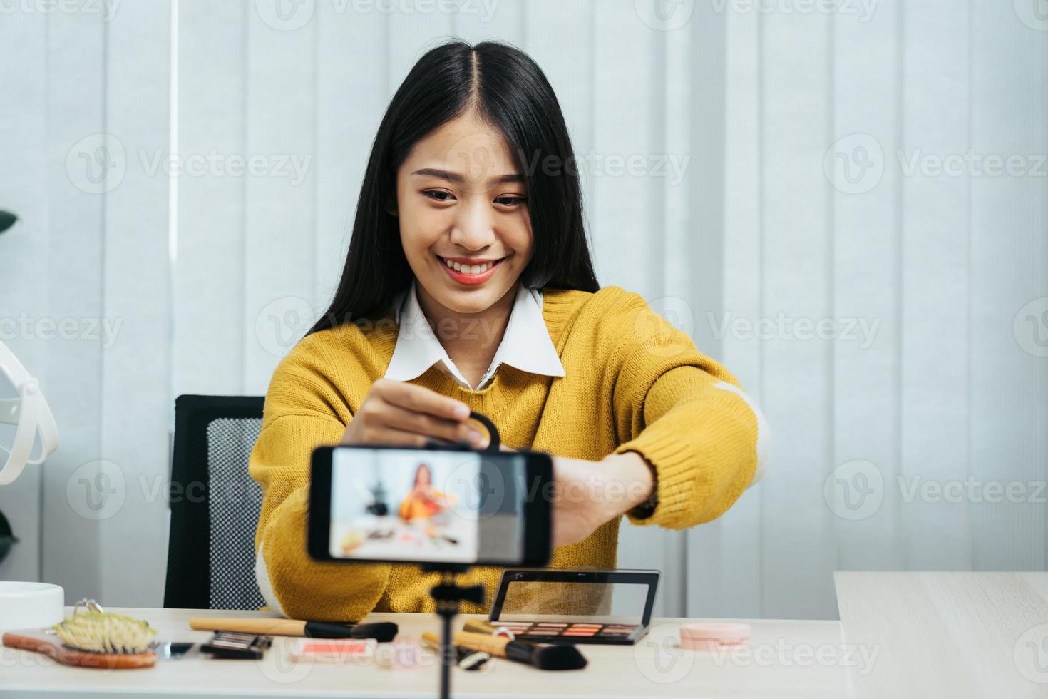 Beautiful asian woman blogger using camera phone recording vlog video live streaming and showing how to make up cosmetics at home. photo