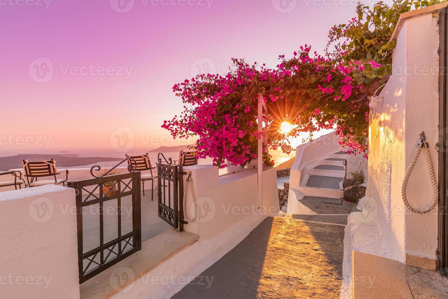 Beautiful view of Caldera and enjoying romantic scenery sunset Aegean sea, Santorini. Couple travel vacation, honeymoon destination. Romance with flowers, two chairs table and sea view. Luxury holiday photo