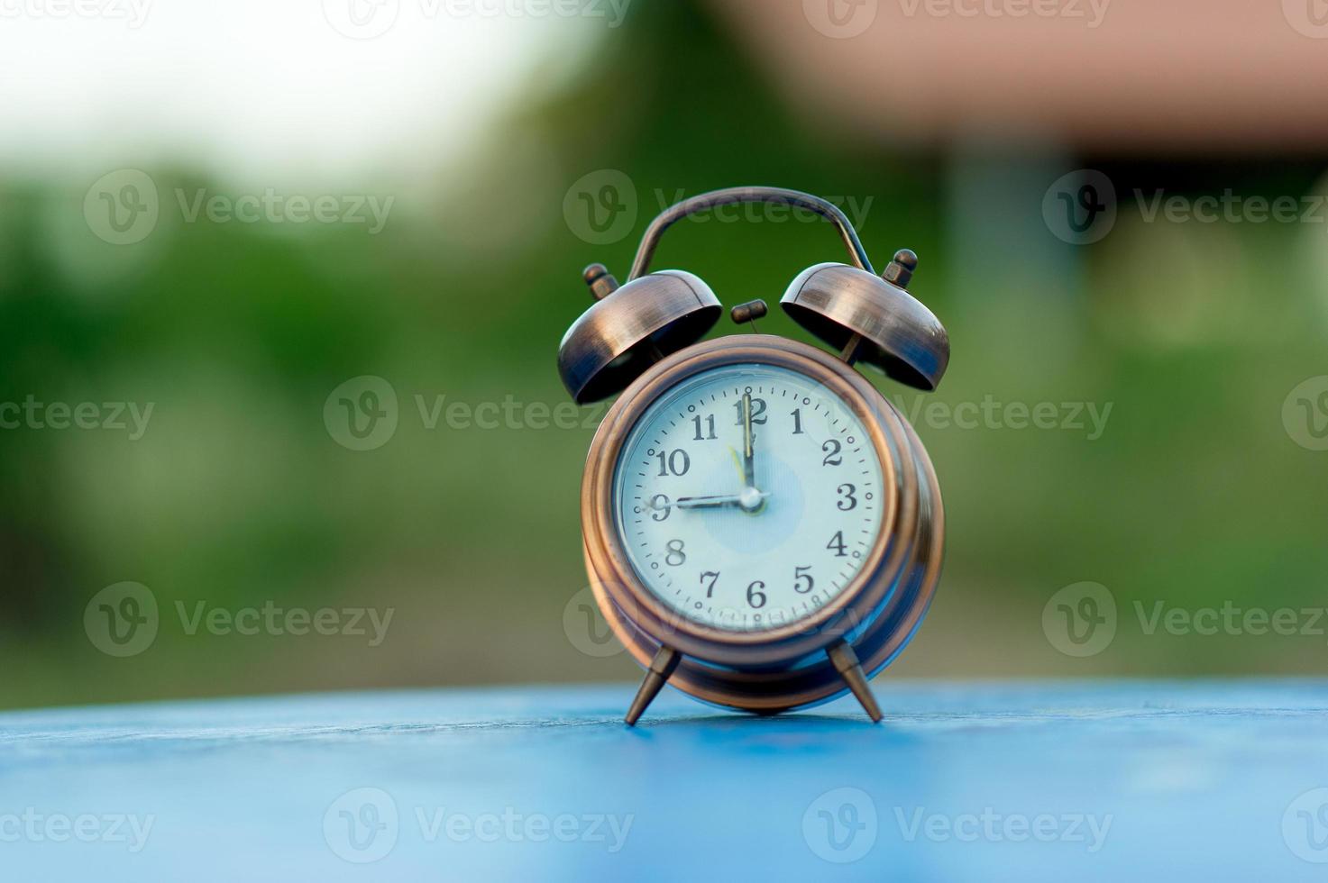 Golden alarm clock picture placed on a blue table, green background Punctual concept With copy space photo