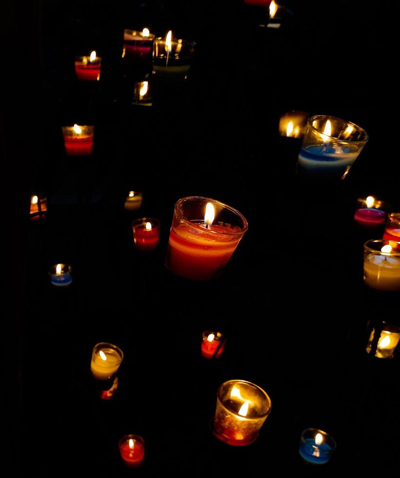 muchas velas aromáticas encendidas están dispuestas en diferentes niveles sobre fondo negro, velas aromáticas para la curación y la relajación, el símbolo de la paz, la oración, el romance, el amor, la muerte y la memoria. foto