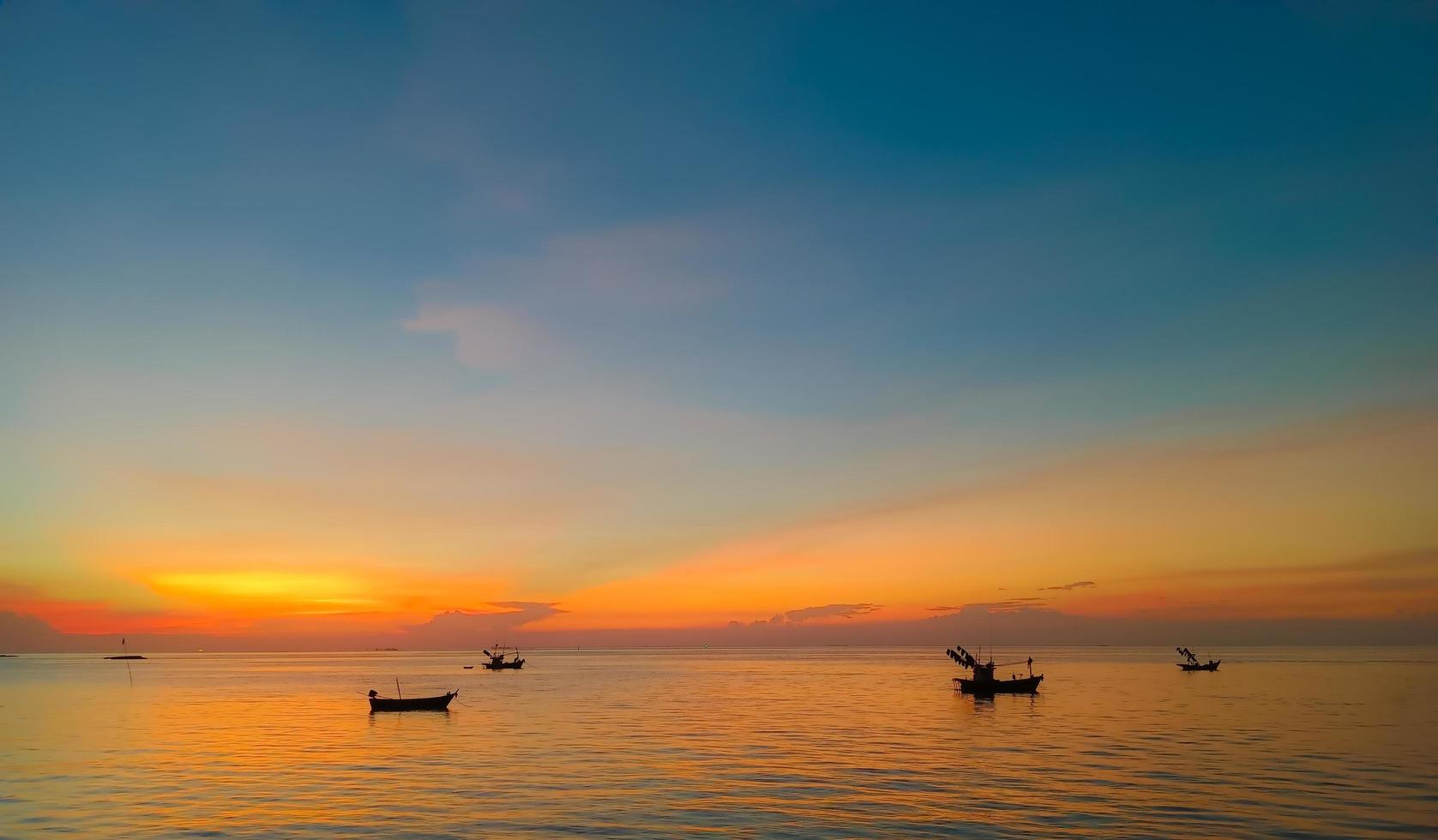 Sky and sea at sunset, local boats floating in the middle of the sea, orange and blue sky reflecting the sea, giving a calm feeling. photo