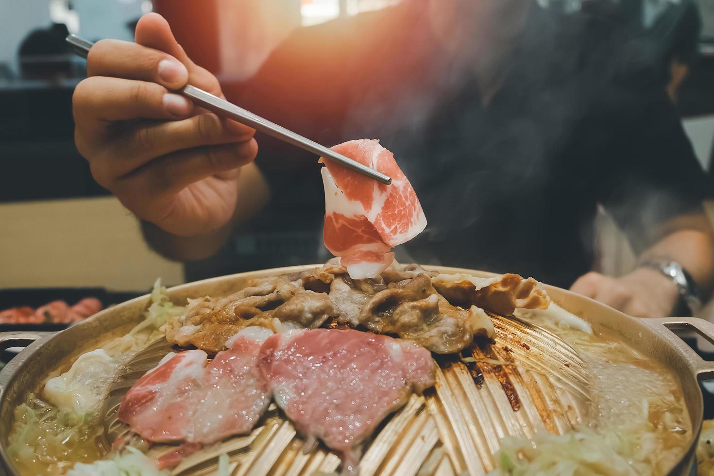 Asian man eating yakiniku food Japanese version of Korean BBQ. Raw meat on a plate and grilled meat with sauce. Wagyu A5 japanese beef which considered as the best beef in the world photo