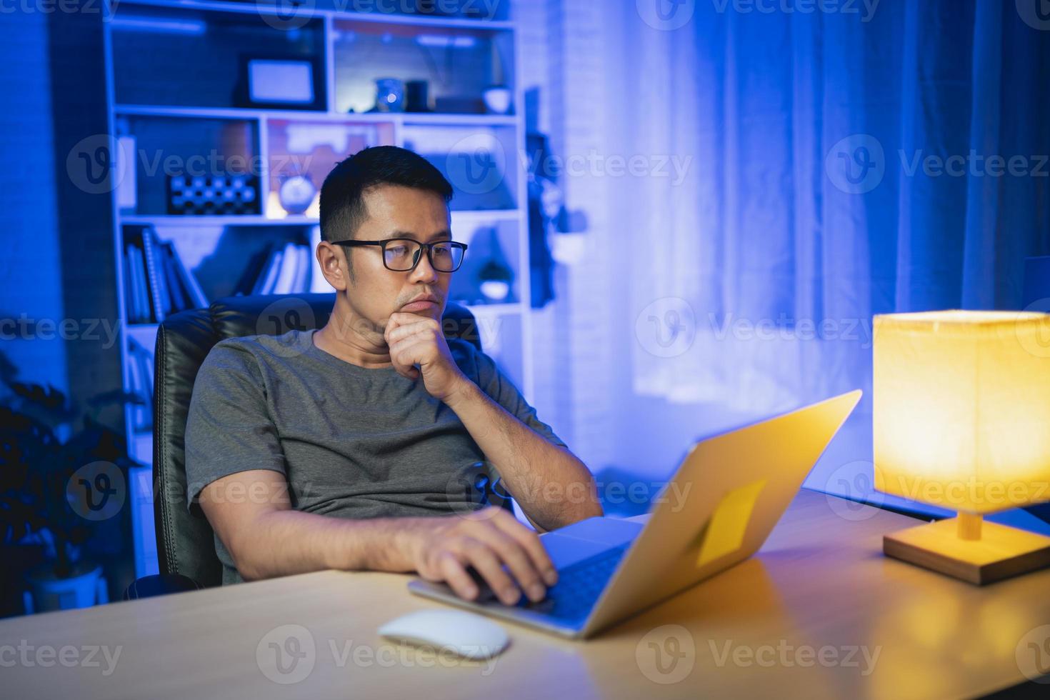 freelance man working on laptop At home at night. Man freelancing, thinking, serious while working at home at night. Freelance work and work from home concept. photo
