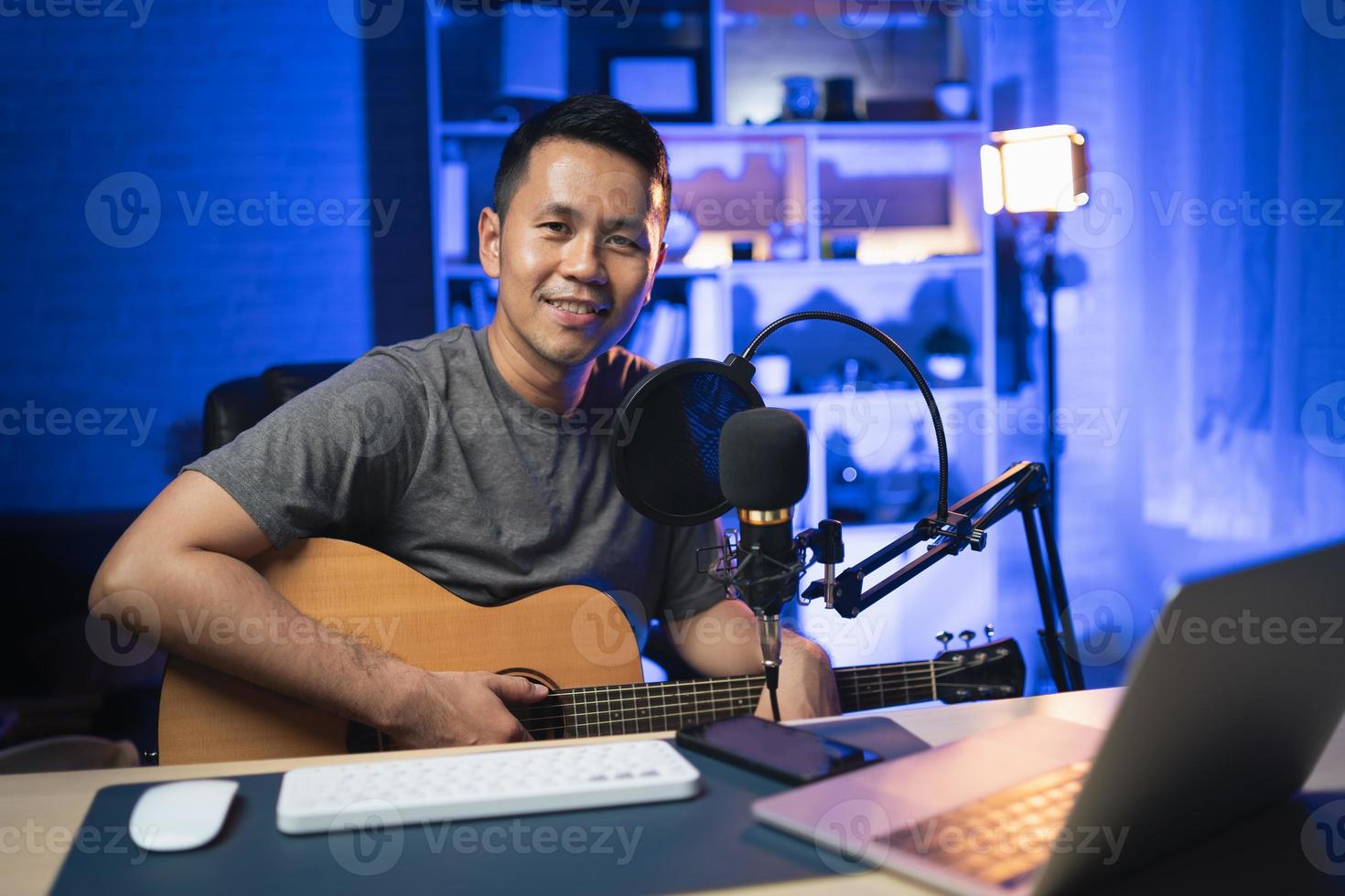 Hombre asiático youtuber transmisión en vivo perfomance tocando guitarra y cantando una canción. hombre asiático enseñando guitarra y cantando en línea. músico grabando música con laptop y tocando guitarra acústica. foto