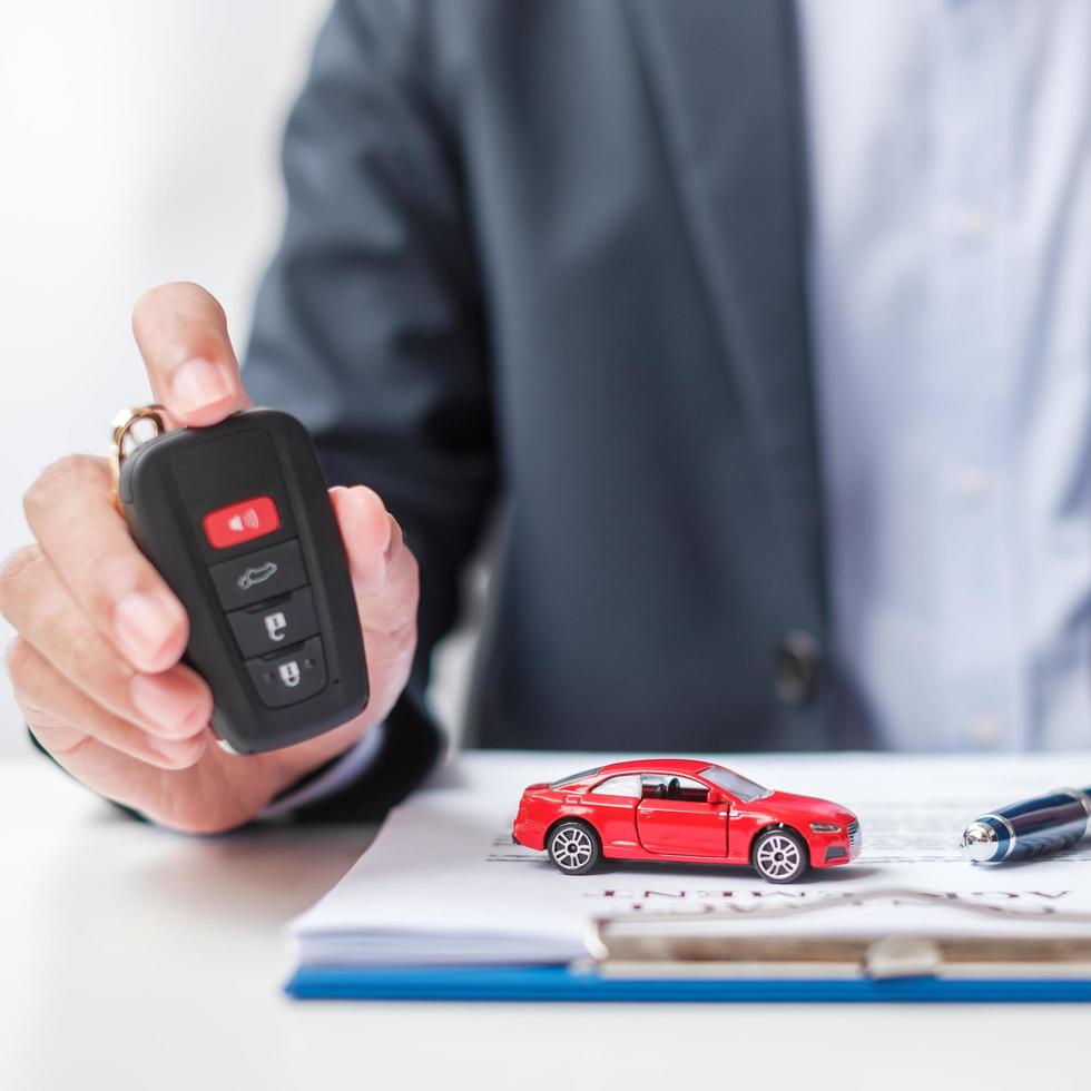 Businessman hand holding remote keyless with car toy, pen and contract document. buy and sale, insurance, rental and contract agreement concepts photo