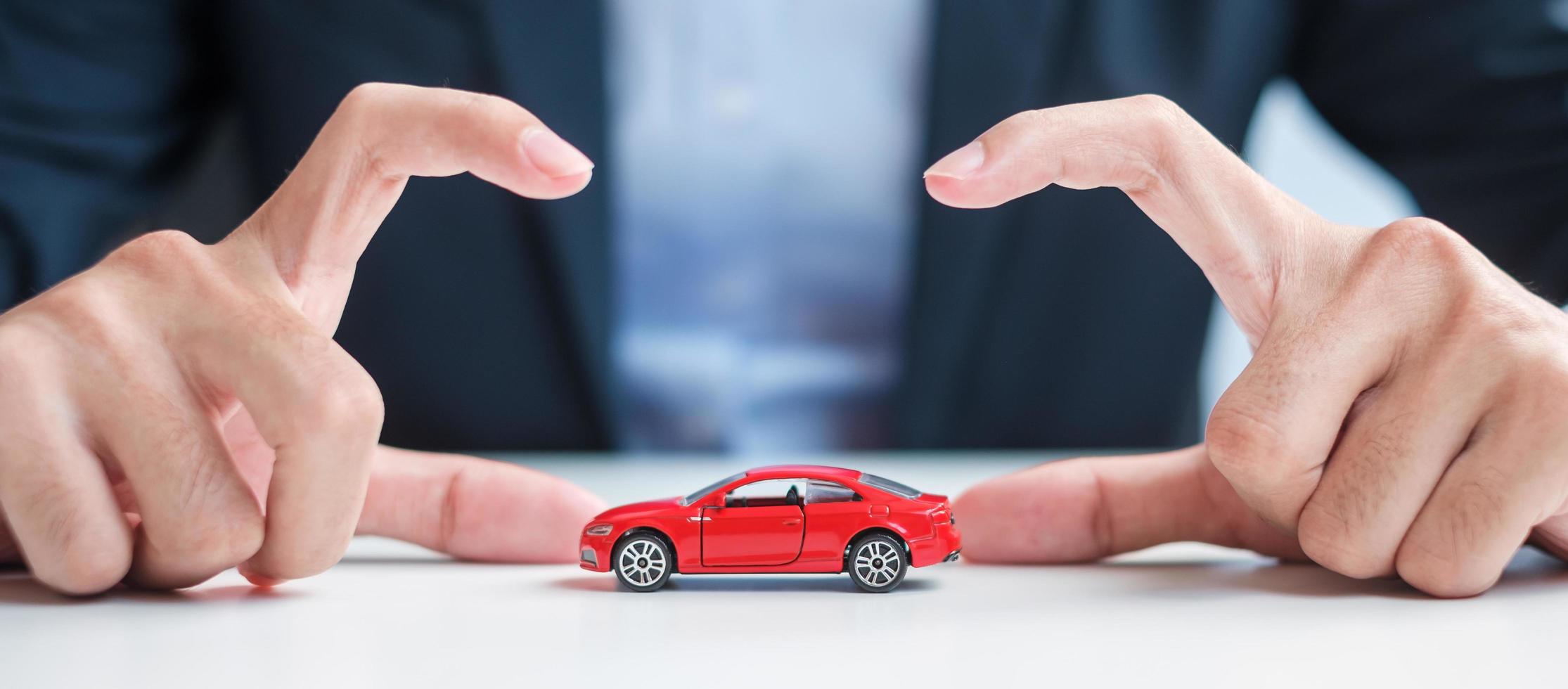 cubierta de mano de hombre de negocios o juguete de coche rojo de protección en la mesa. seguro de automóvil, garantía, reparación, concepto financiero, bancario y monetario foto