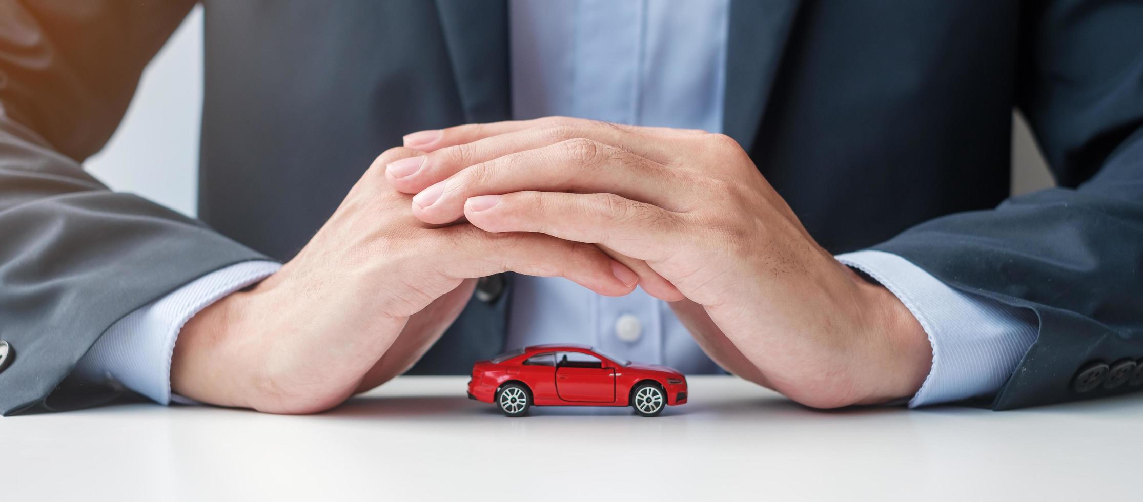 Businessman hand cover or protection red car toy on table. Car insurance, warranty, repair, Financial, banking and money concept photo