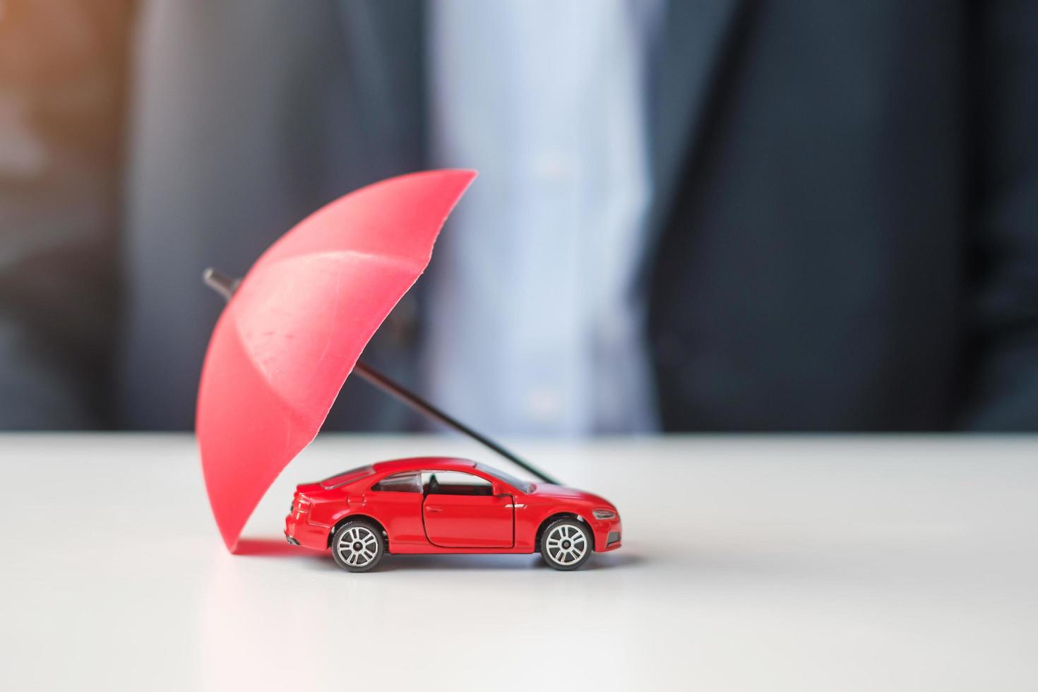 Businessman hand holding umbrella and cover  red car toy on table. Car insurance, warranty, repair, Financial, banking and money concept photo