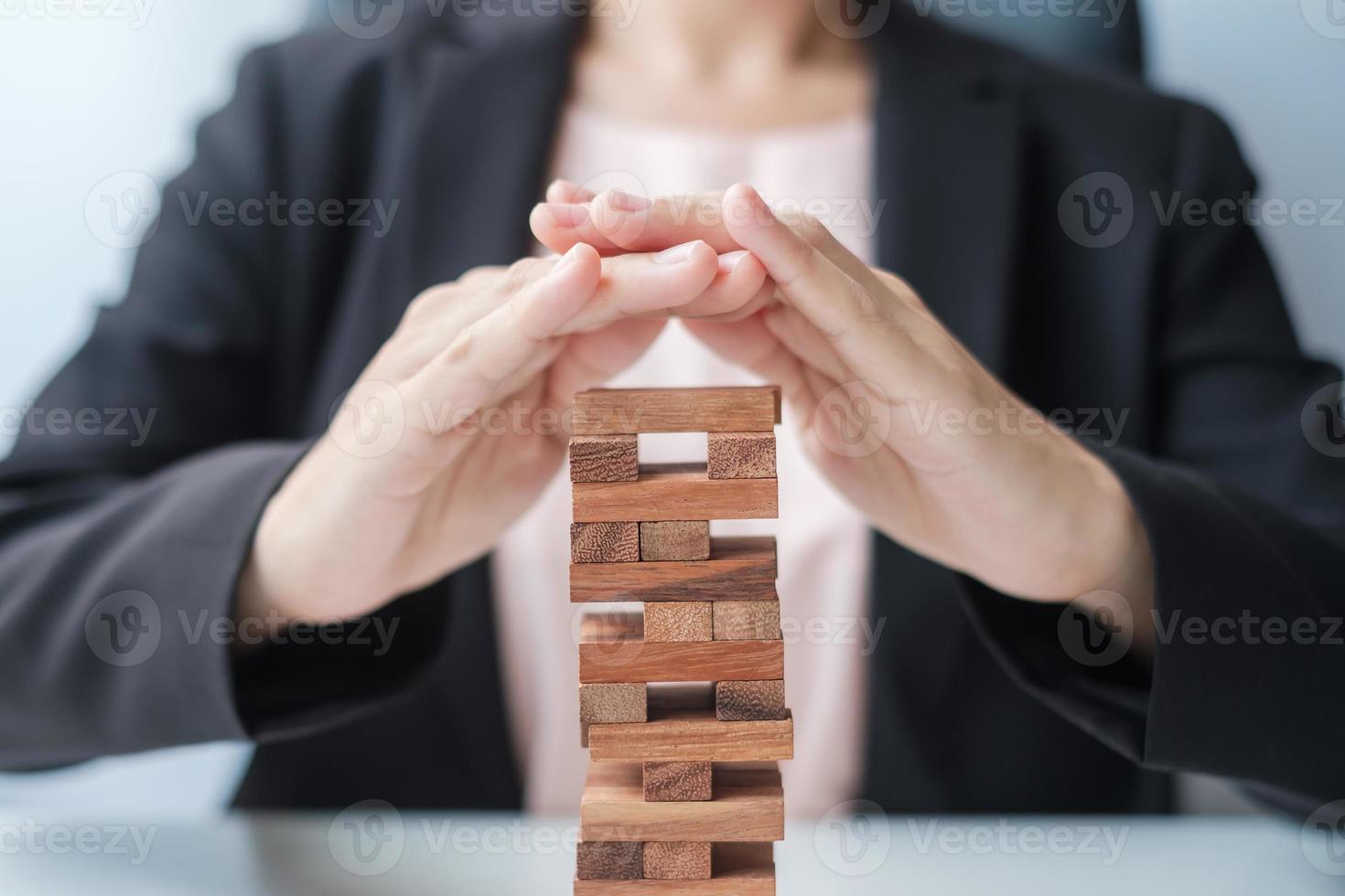 bloque de madera de la cubierta de la mano de la empresaria en la torre. conceptos de planificación empresarial, gestión de riesgos, soluciones, seguros y estrategia foto