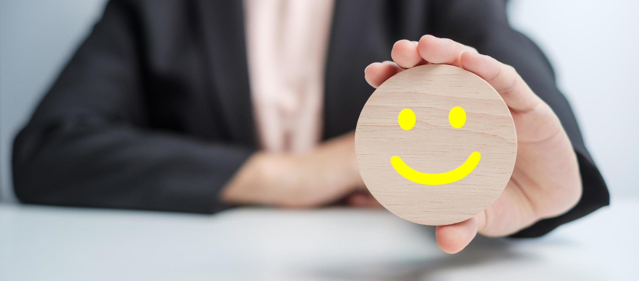 mano sujetando el bloque de cara de sonrisa. el cliente elige el emoticono para las reseñas de los usuarios. calificación de servicio, clasificación, revisión del cliente, satisfacción, estado de ánimo, salud mental y concepto de retroalimentación foto