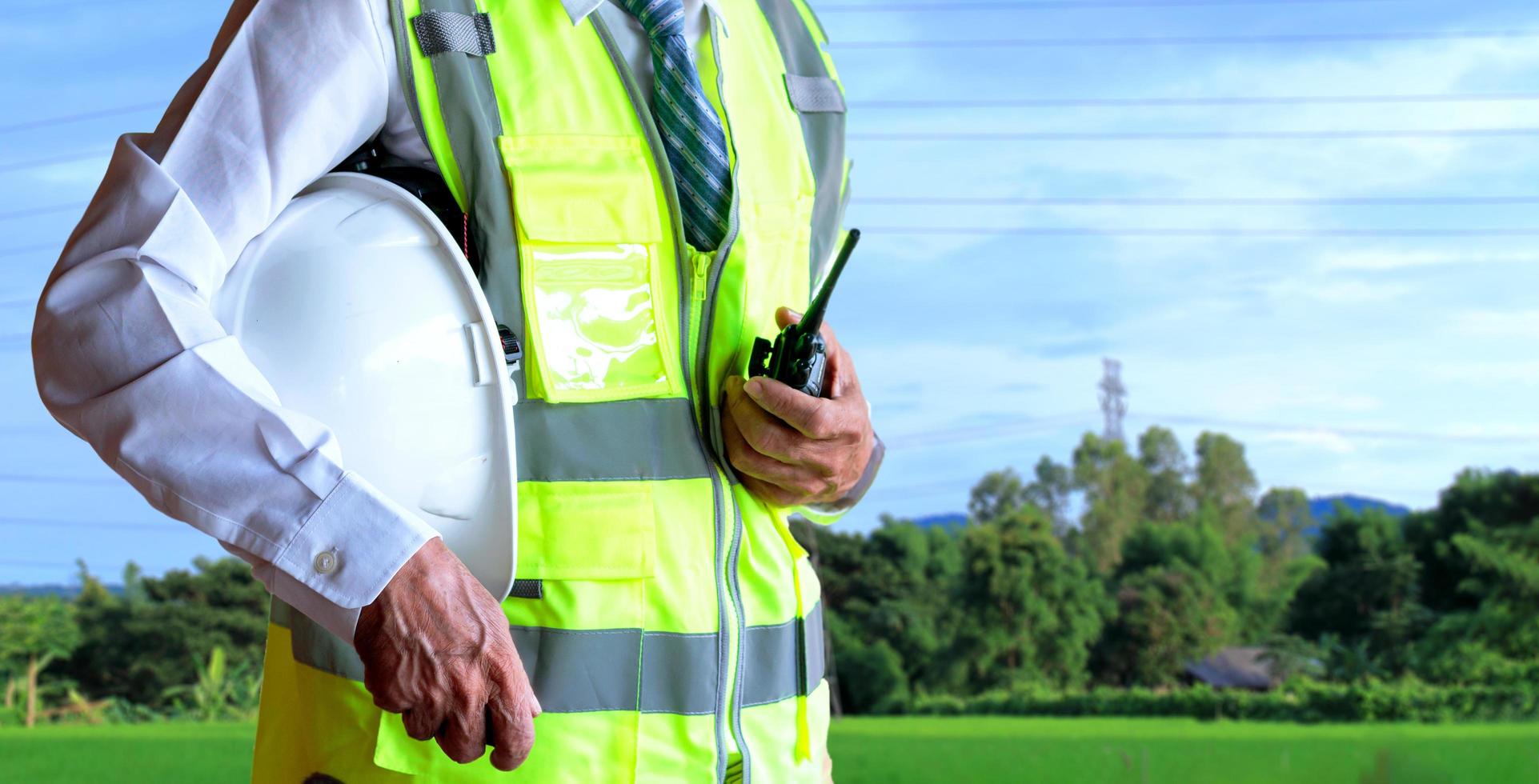 Engineer or businessman holding helmet with walkie-talkie on sky and field background photo