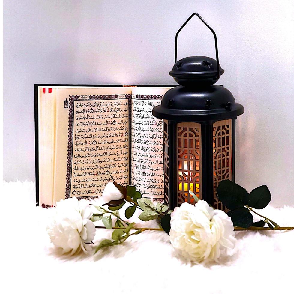 The lantern of Ramadan is black in color, luminous, decorated with wooden motifs, next to the Holy Quran, with a few white roses photo