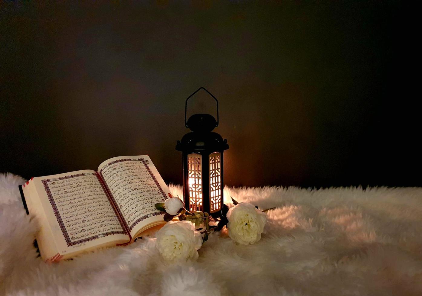 The lantern of Ramadan is black in color, luminous, decorated with wooden motifs, next to the Holy Quran, with a few white roses photo