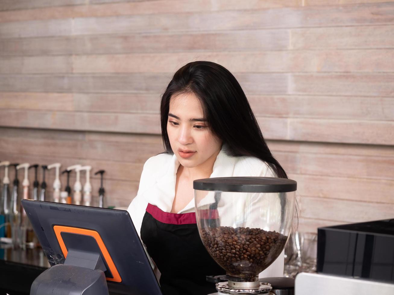 bella mujer asiática propietaria de una cafetería y una barista parada en el bar y revisando los pedidos de los clientes en línea desde una computadora en la cafetería foto