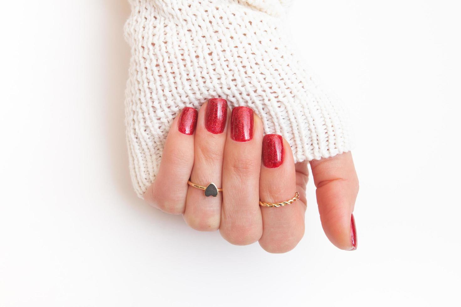 Manicure gel polish of red color with sparkles on female hand with rings photo