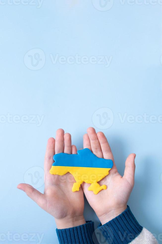 Ukrainian plasticine map of yellow-blue color of the national flag of Ukraine in a childs hands, top view. Vertical format photo