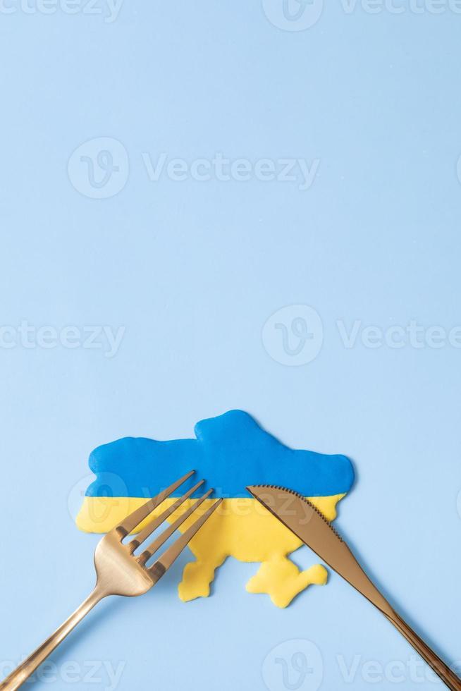 Yellow and blue Ukrainian map with fork and knife, top view.Aggression against Ukraine concept. Copy space vertical format photo