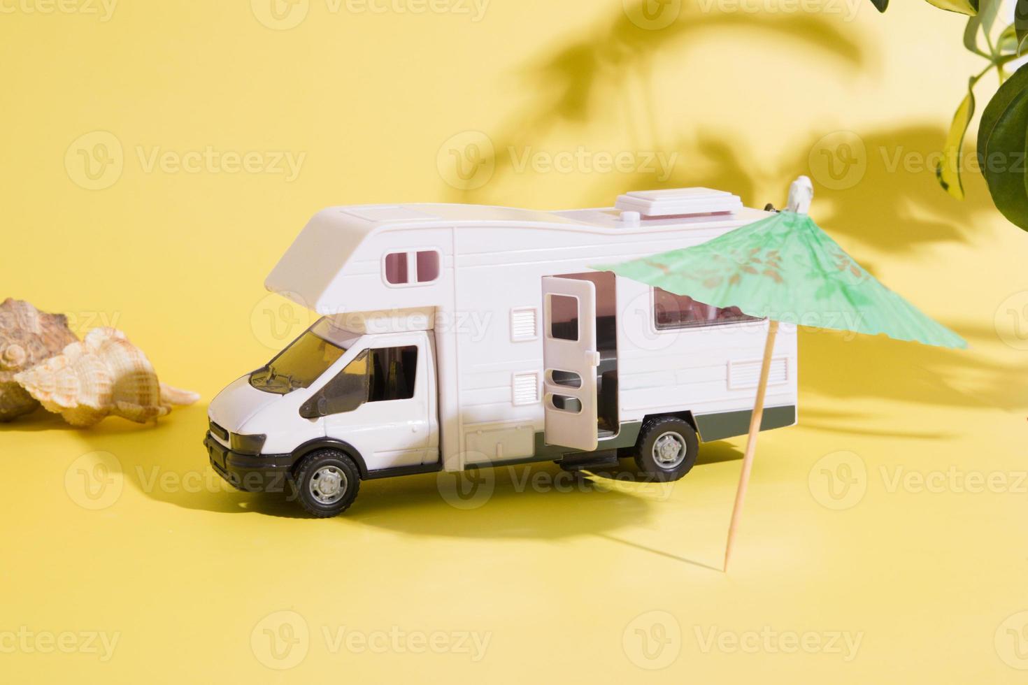 toy travel van with umbrella on yellow background with plants shadow. Minimalistic summer family travel concept photo