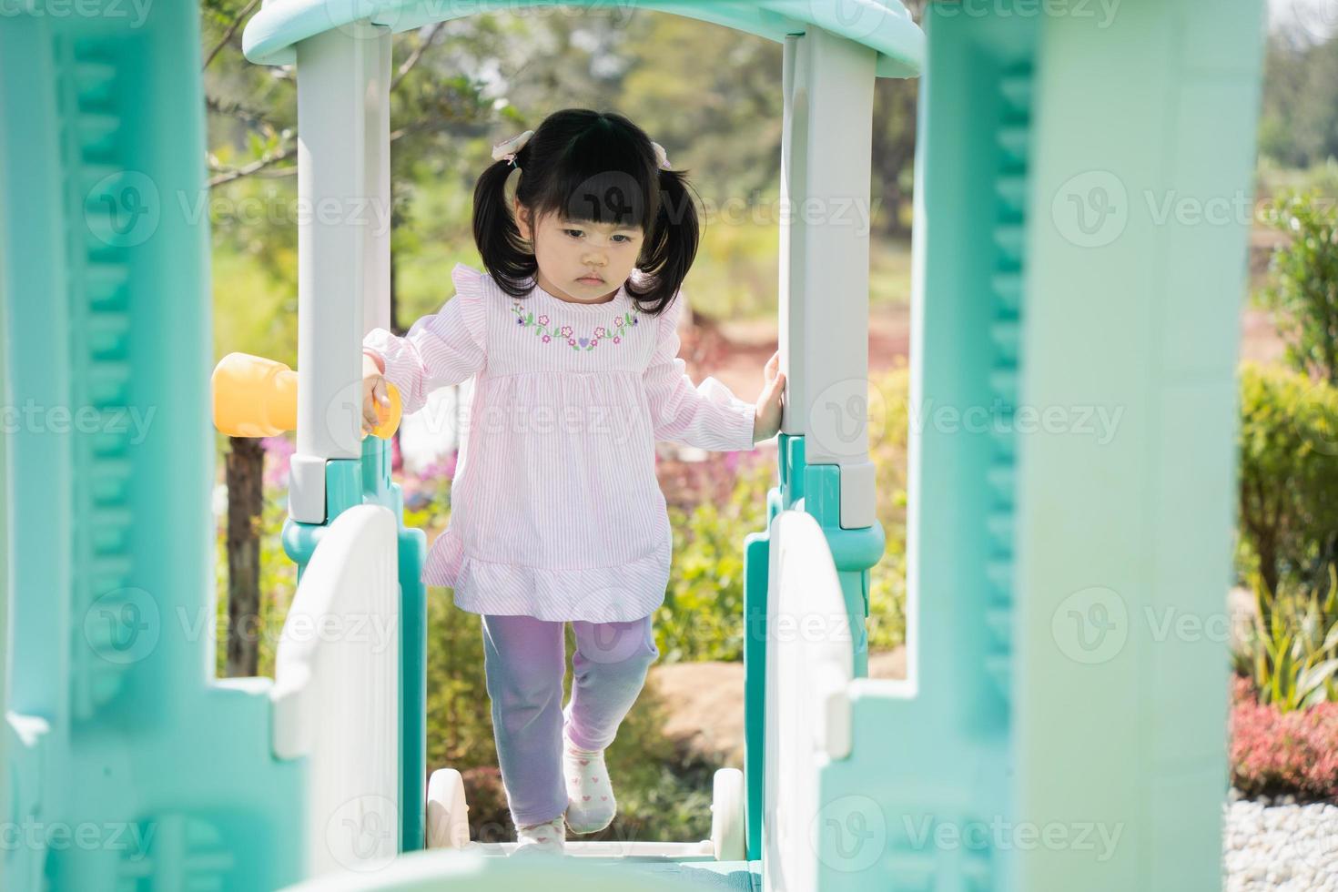 Cute asian girl play on school or kindergarten yard or playground. Healthy summer activity for children. Little asian girl climbing outdoors at playground. Child playing on outdoor playground. photo