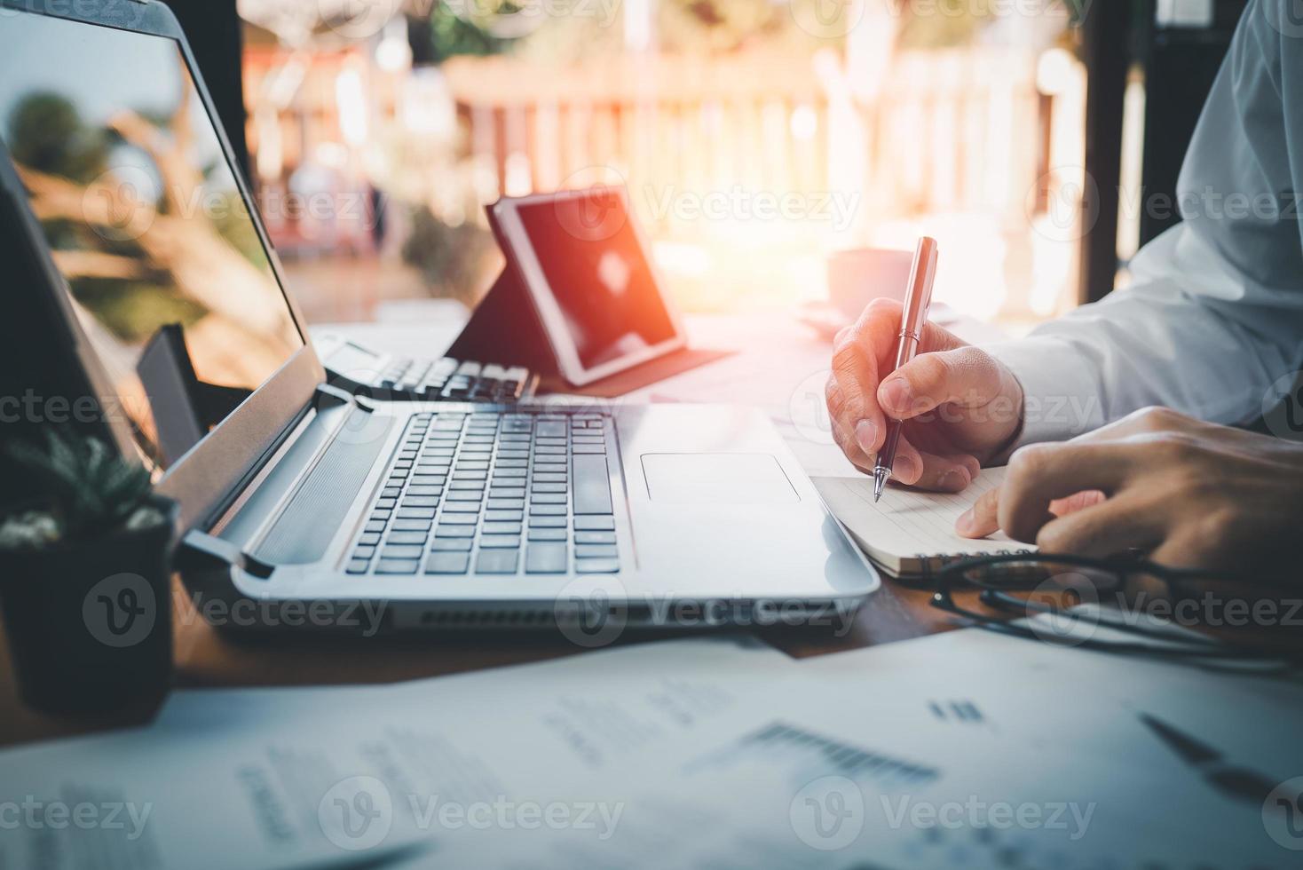 closeup hands of business man working on laptop and using pen making notices in her notebook on wooden table with a cup of coffee. Business concept photo