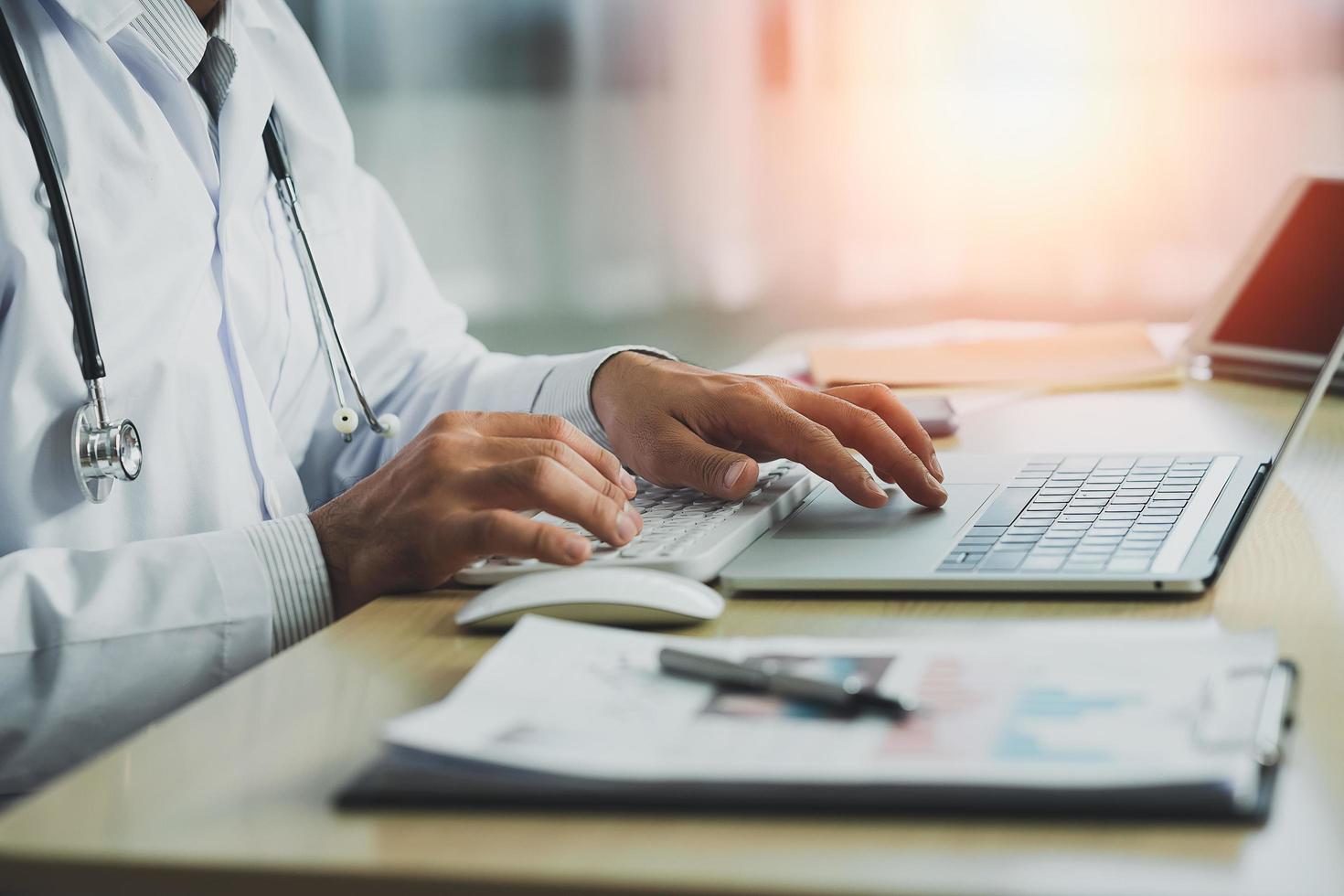 Doctor working with chart paper and laptop computer looking graph. Male doctor work at office hospital. Health hospital concept photo