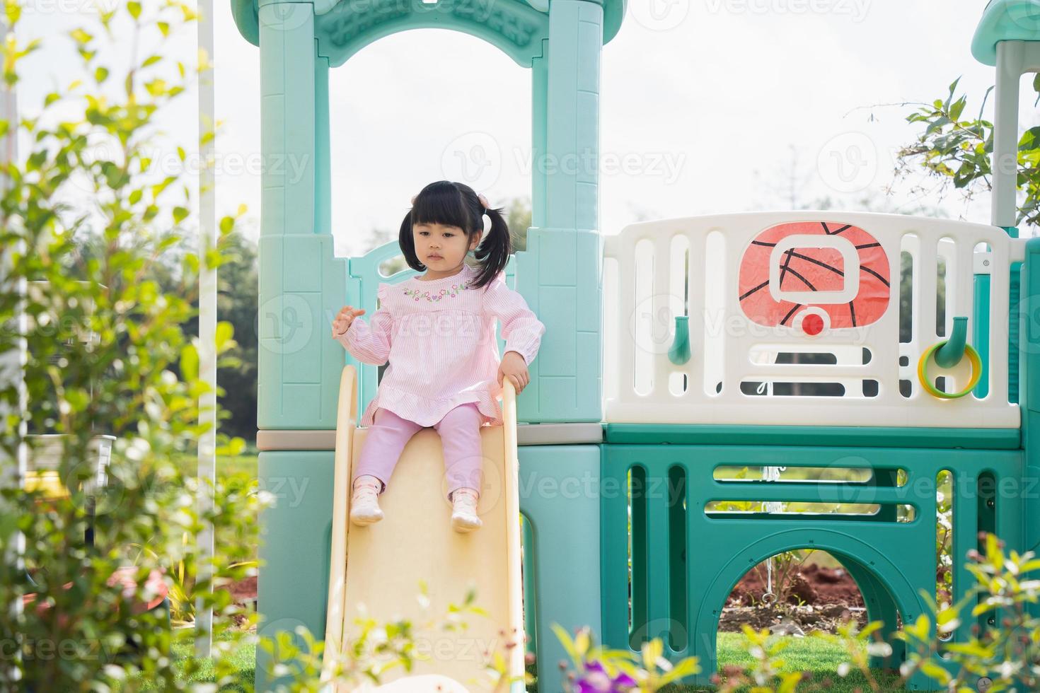 linda chica asiática juega en la escuela o en el jardín de infantes o en el patio de recreo. Actividad de verano saludable para niños. niña asiática escalando al aire libre en el patio de recreo. niño jugando en el patio de recreo al aire libre. foto