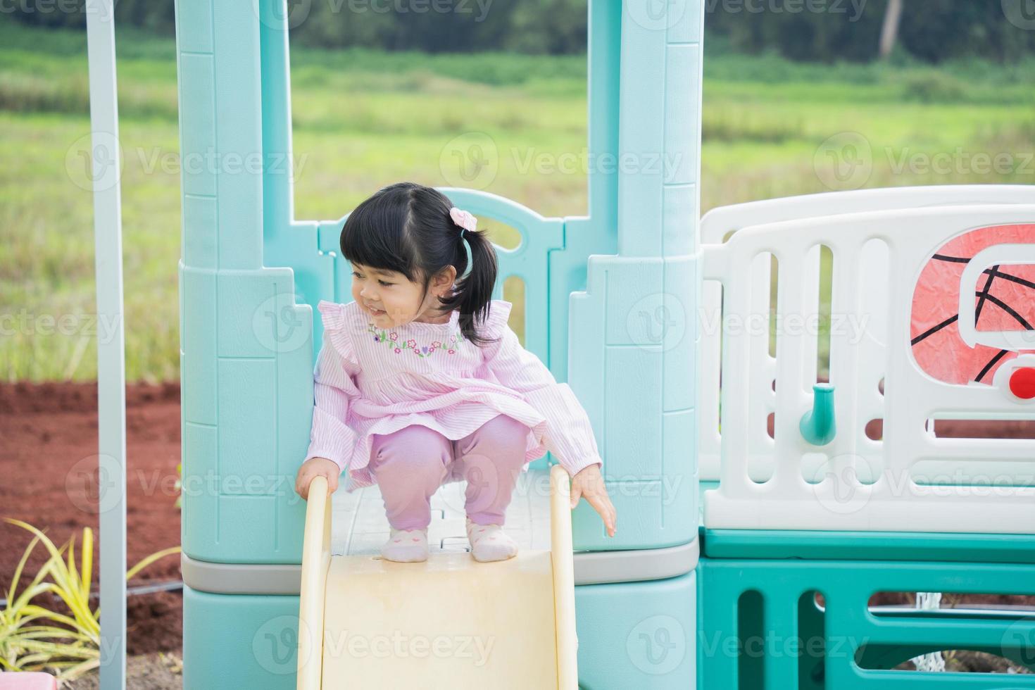 Cute asian girl play on school or kindergarten yard or playground. Healthy summer activity for children. Little asian girl climbing outdoors at playground. Child playing on outdoor playground. photo