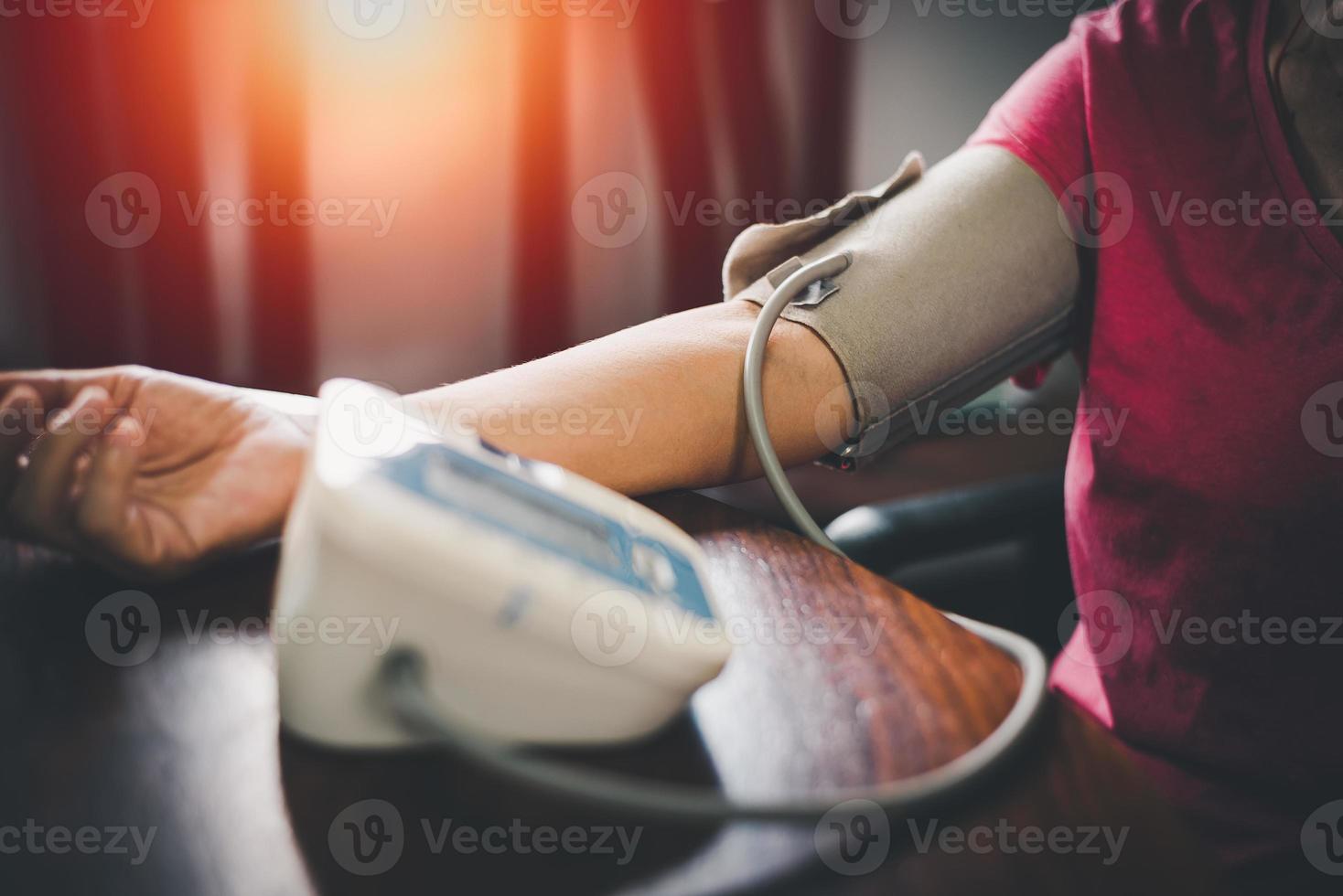 bíceps de la parte superior del brazo de la mujer mayor en el manguito. anciana jubilada midiendo manualmente la presión arterial, usando una máquina de tonómetro digital en casa. atención médica, concepto de tratamiento de enfermedades. foto