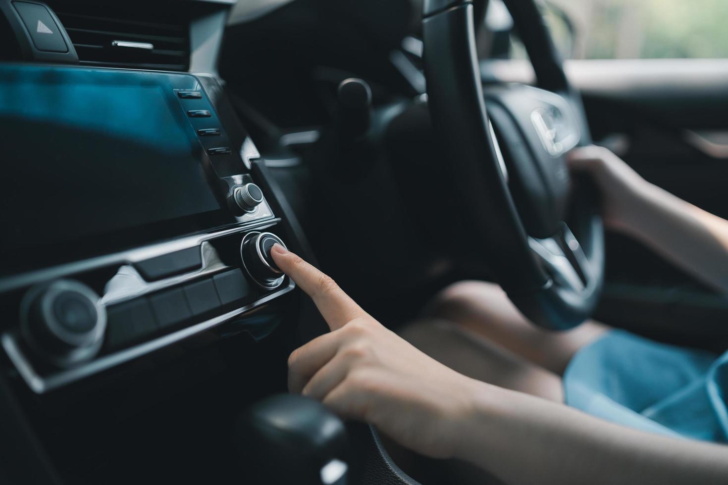 Woman adjusting the air conditioner button in the car. Close up hand touch air conditioner button to making cool in car. Woman turn on the audio button in car. photo