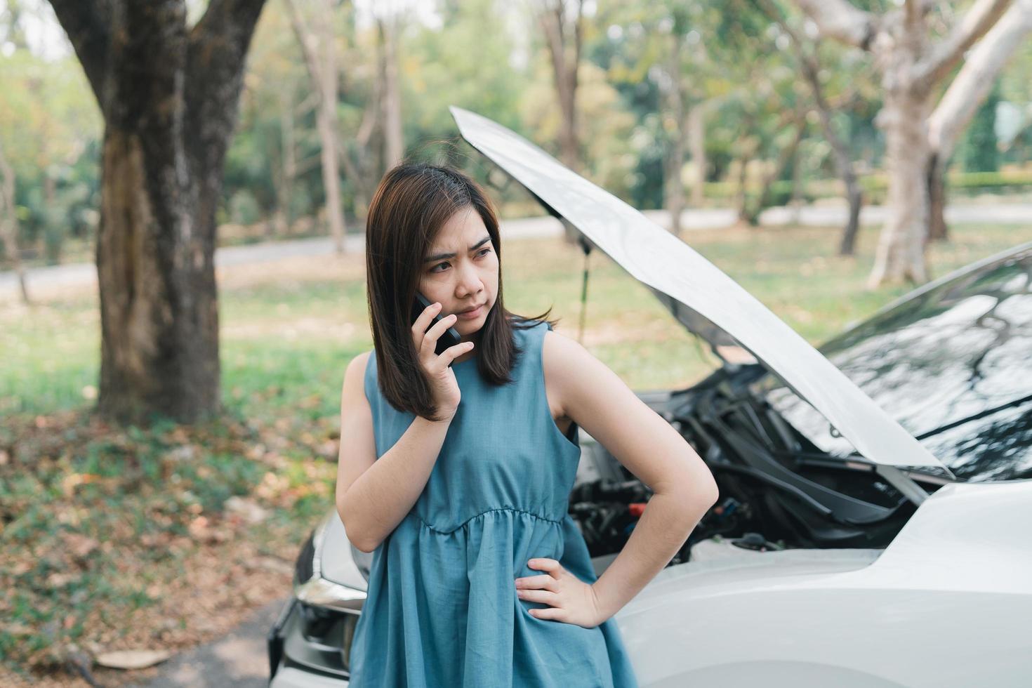 Asian woman calling garage after car breaks down. woman opening car hood and call to insurance or someone to help after the car breaks down, park on the side of the road. Transportation concept. photo