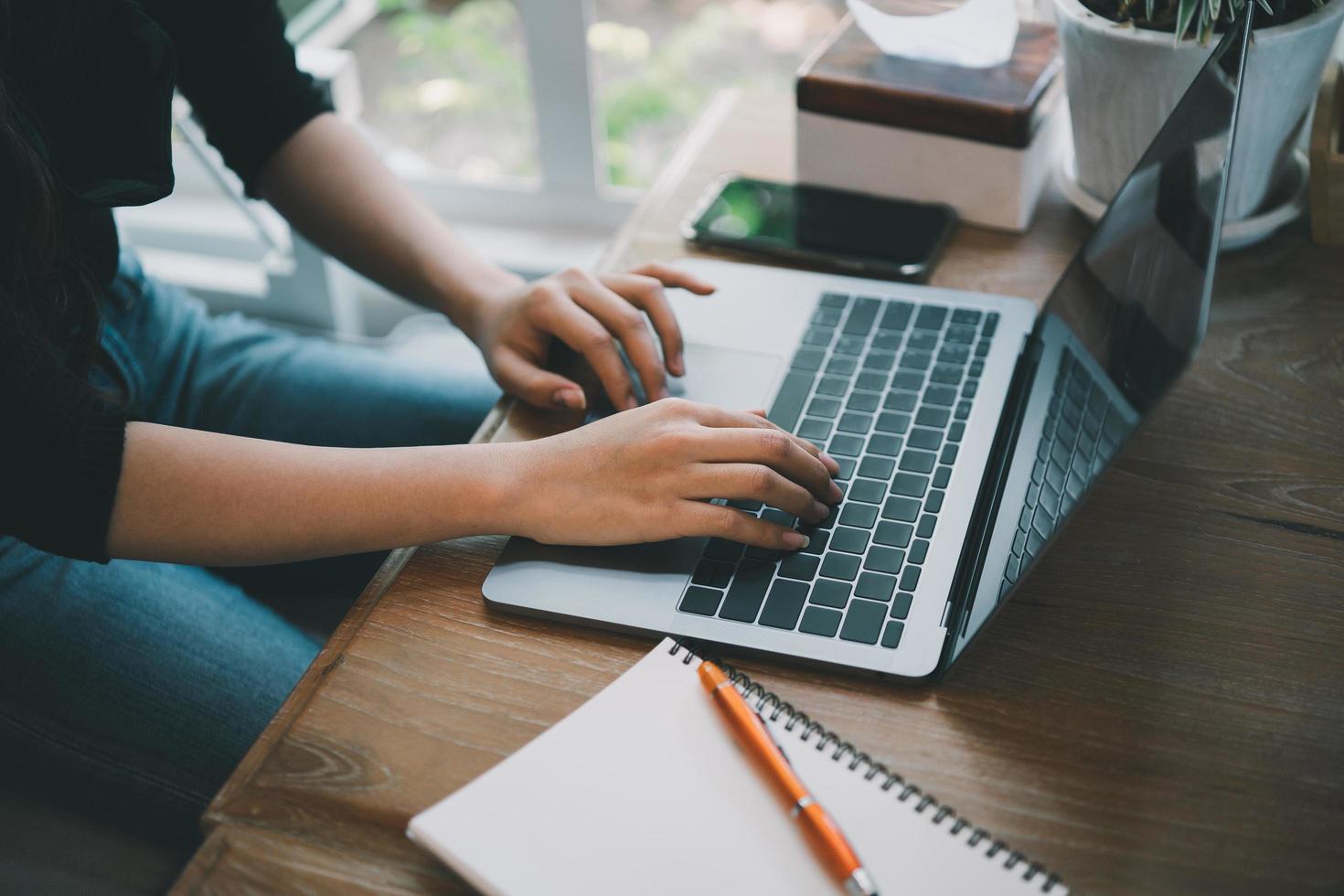 cierre las manos de una mujer de negocios que trabaja en una laptop y usa un bolígrafo para hacer notas en su cuaderno sobre una mesa de madera con una taza de café. concepto de negocio foto