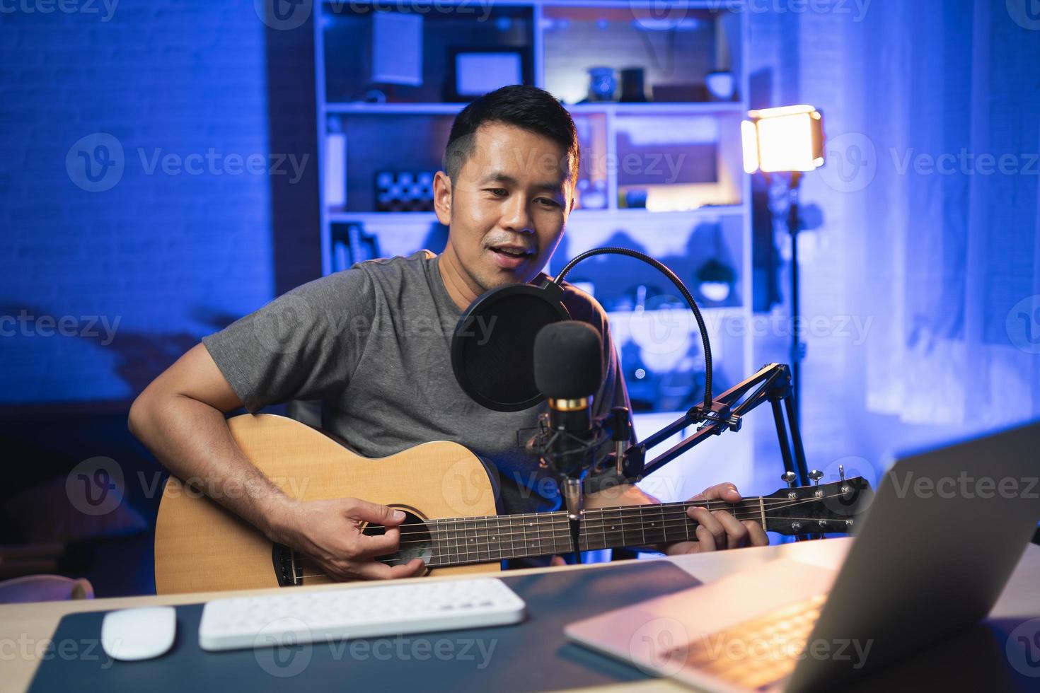 Asian man youtuber live streaming perfomance playing guitar and sing a song. Asian man teaching guitar and singing online. Musician recording music with laptop and playing acoustic guitar. photo