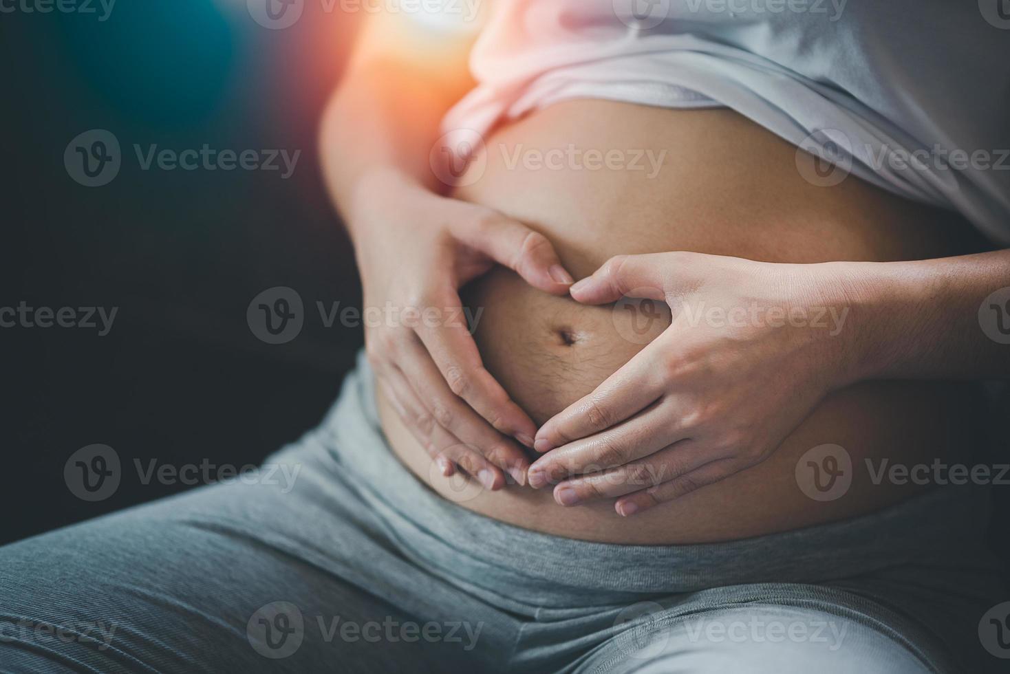 Pregnant woman holding hands in heart shape on belly at home.pregnant woman making heart with her hands, closeup. photo