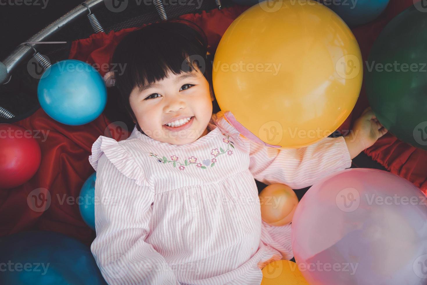 linda chica asiática juega en la escuela o en el jardín de infantes o en el patio de recreo. niña asiática jugando pelota de colores en el patio de recreo. niño jugando en el patio de recreo al aire libre. foto