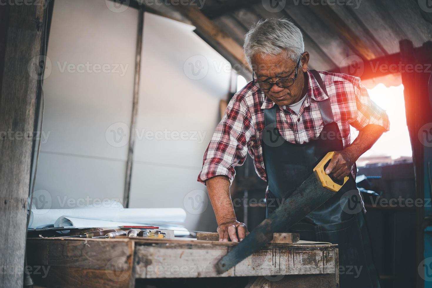 carpintero de edad avanzada que usa sierra trabajando en artesanía de madera en el taller para producir material de construcción o muebles de madera. foto