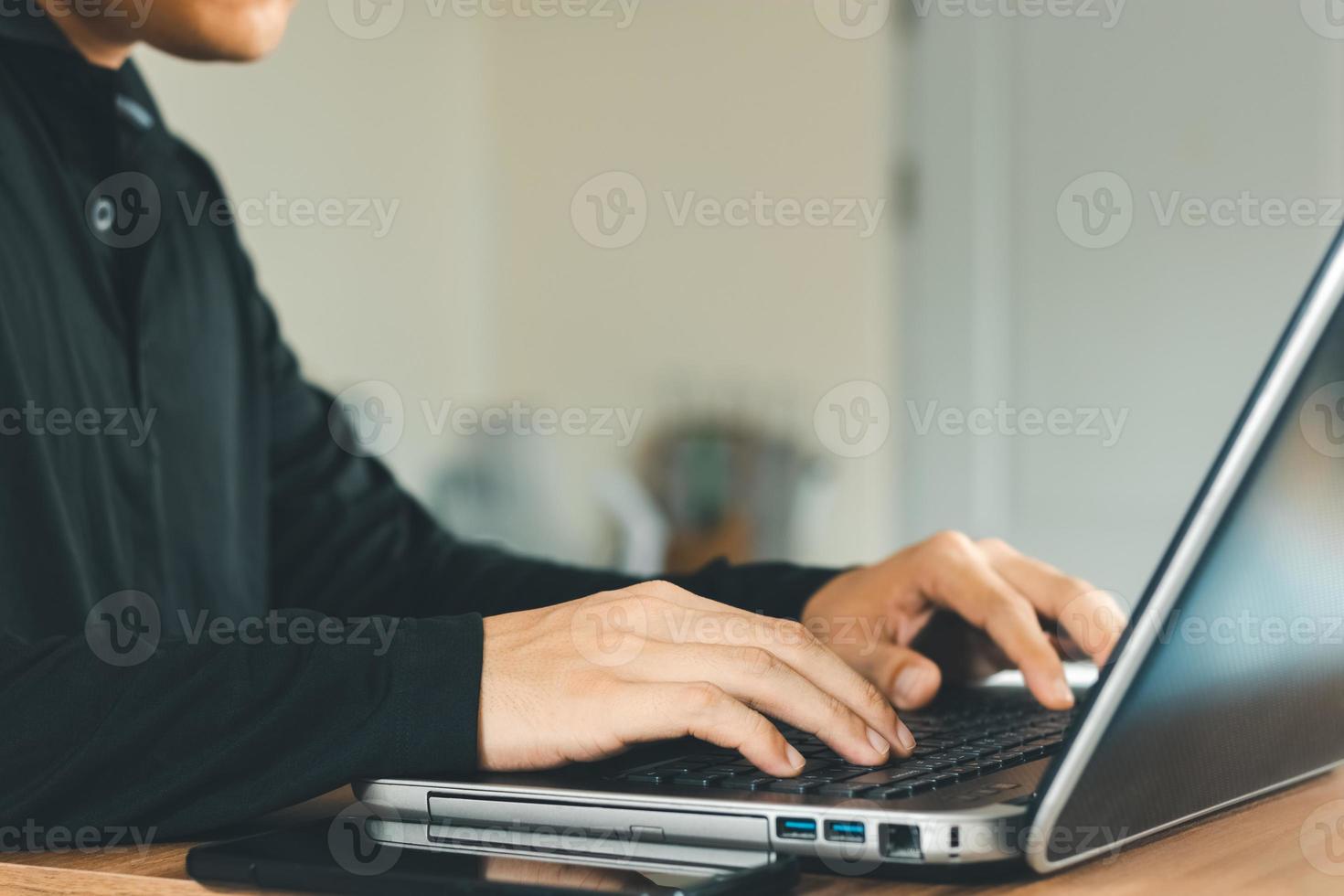 young man using  laptop computer and  mobile phone When looking for financial information in business, work at the desk. Writing with a pen, studying remotely from home and working from home. photo