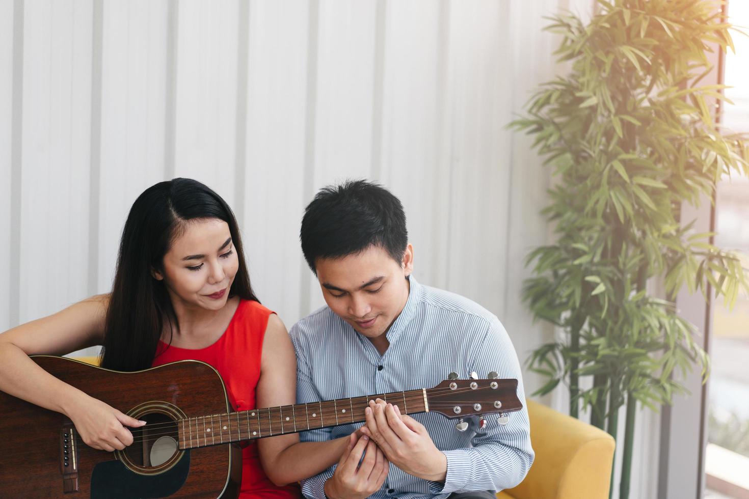 pareja asiática romántica tocando la guitarra juntos. Actividad sencilla en casa. foto