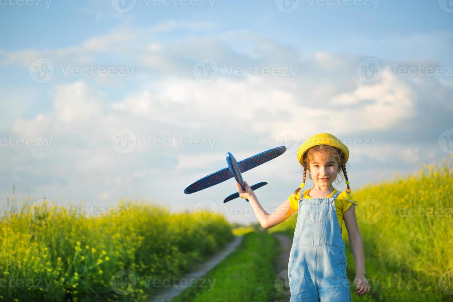 Girl in a yellow panama hat launches a toy plane into the field. Summer time, happy childhood, dreams and carelessness. Air tour from a travel agency on a trip, flight, adventure and vacation. photo