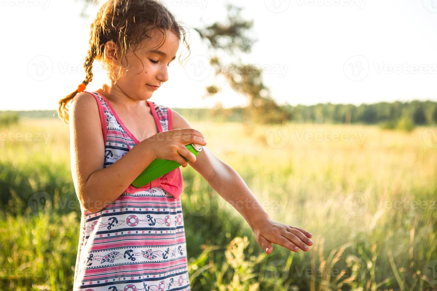 la chica rocía spray para mosquitos en la piel en la naturaleza que le muerde las manos y los pies. Protección contra picaduras de insectos, repelente seguro para niños. recreación al aire libre, contra las alergias. Hora de verano foto