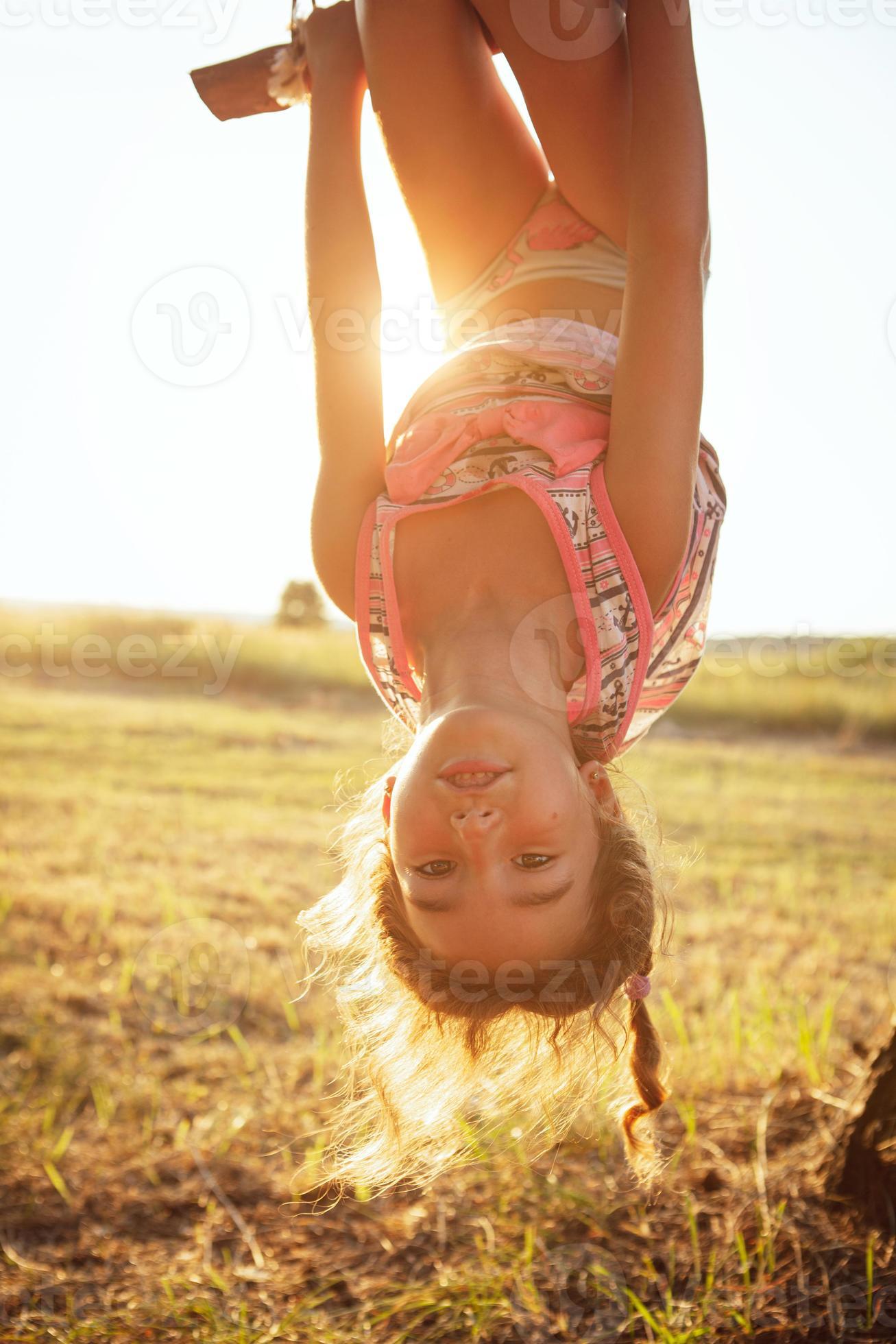 The girl is hanging upside down on a tree in summer in orange sunlight and  a light dress. Summer time, heat, childhood. Funny portrait with disheveled  hair 6699807 Stock Photo at Vecteezy