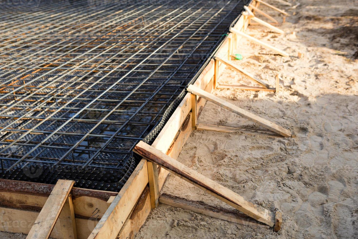 Iron fittings on a wooden formwork with laid pipes are the basis for pouring the foundation of the house with a concrete slab. Construction of cottages, design, engineering communications. photo