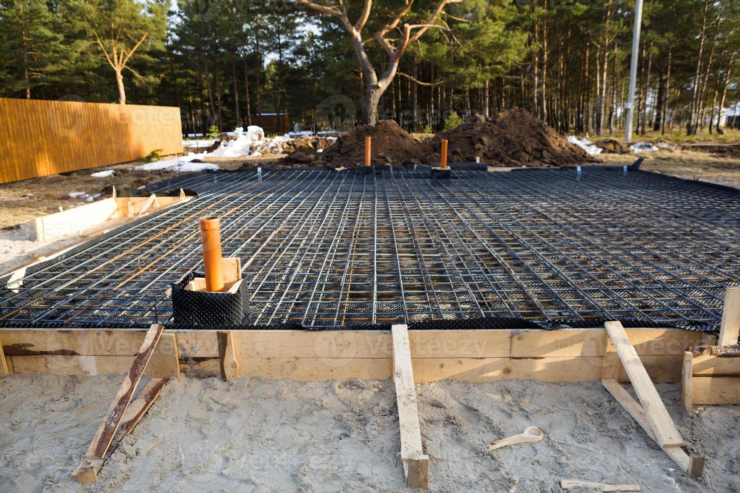 Iron fittings on a wooden formwork with laid pipes are the basis for pouring the foundation of the house with a concrete slab. Construction of cottages, design, engineering communications. photo